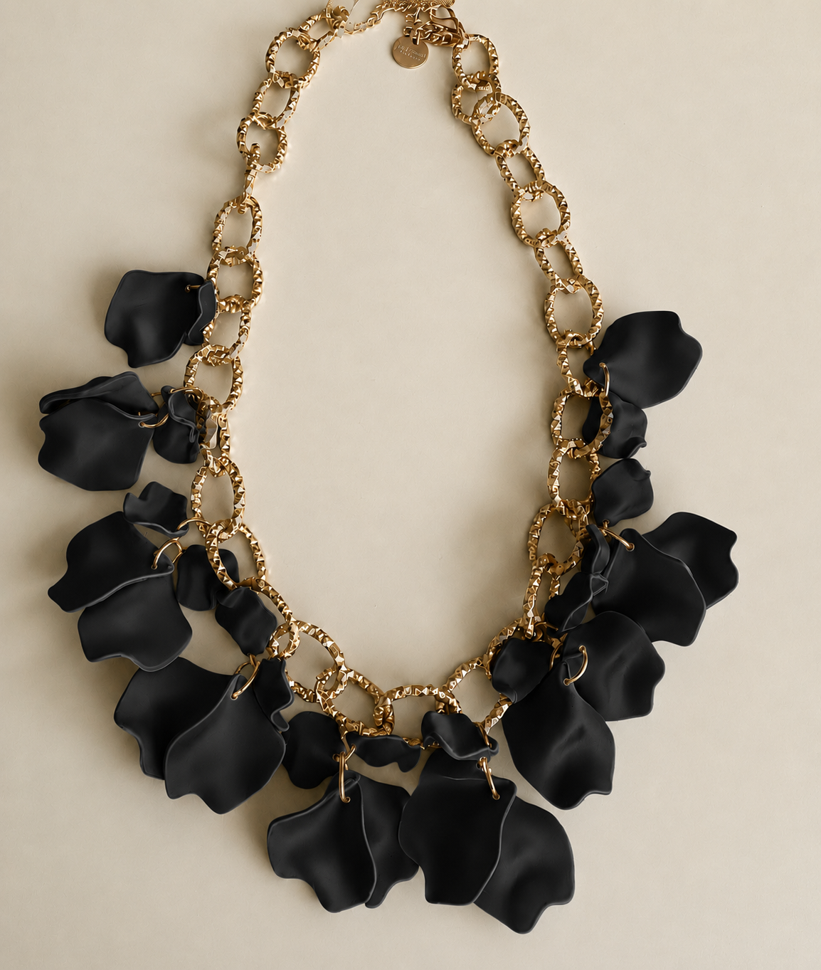 halsband svarta löv med guldfärgad kedja och flera svarta lövformade hängen på beige bakgrund