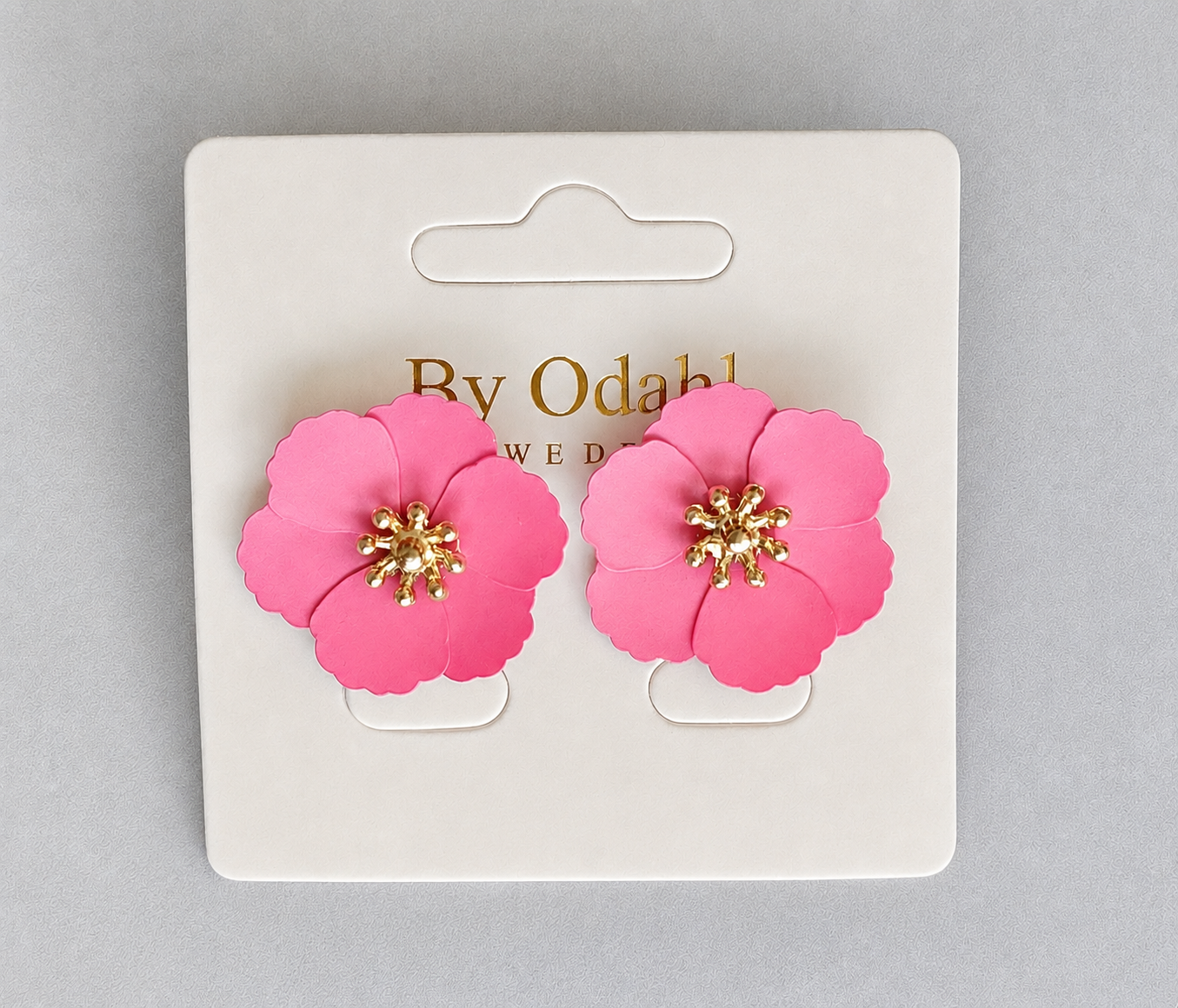 två rosa blomma örhängen med guldtonad mitt monterade på ett vitt displaykort