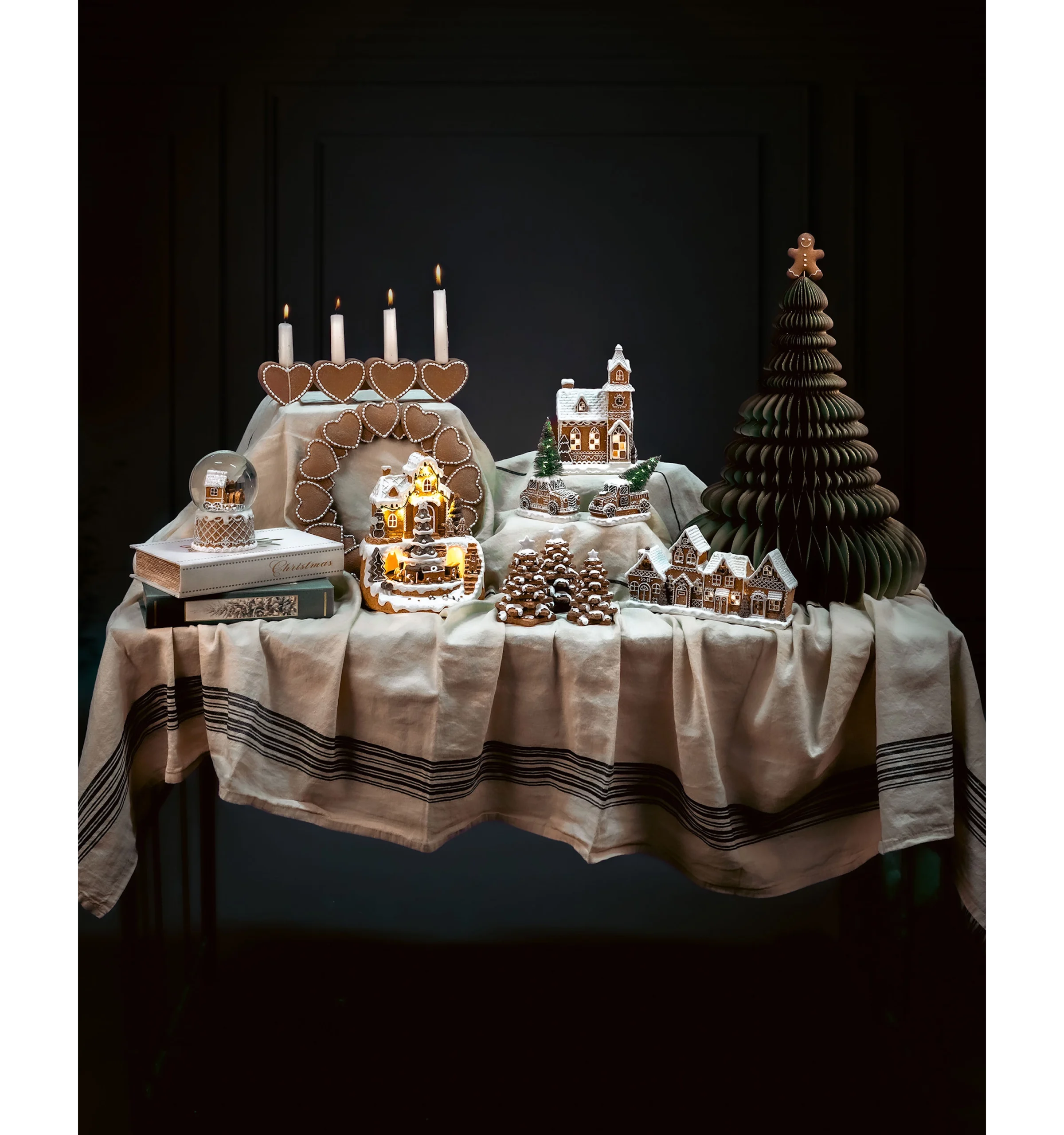 ljuslykta pepparkakslastbil i upplyst julby på dukat bord med pepparkakshus, snöglob och pappersgran