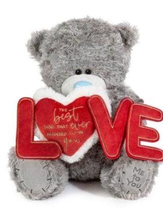 Grå nalle med blå nos som sitter och håller ett rött hjärta samt röda bokstäver som bildar LOVE – nalle med hjärta.