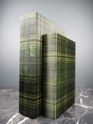 två exemplar av en grön rutig boklåda i olika storlekar stående upprätt på en mörk marmoryta mot ljusgrå bakgrund