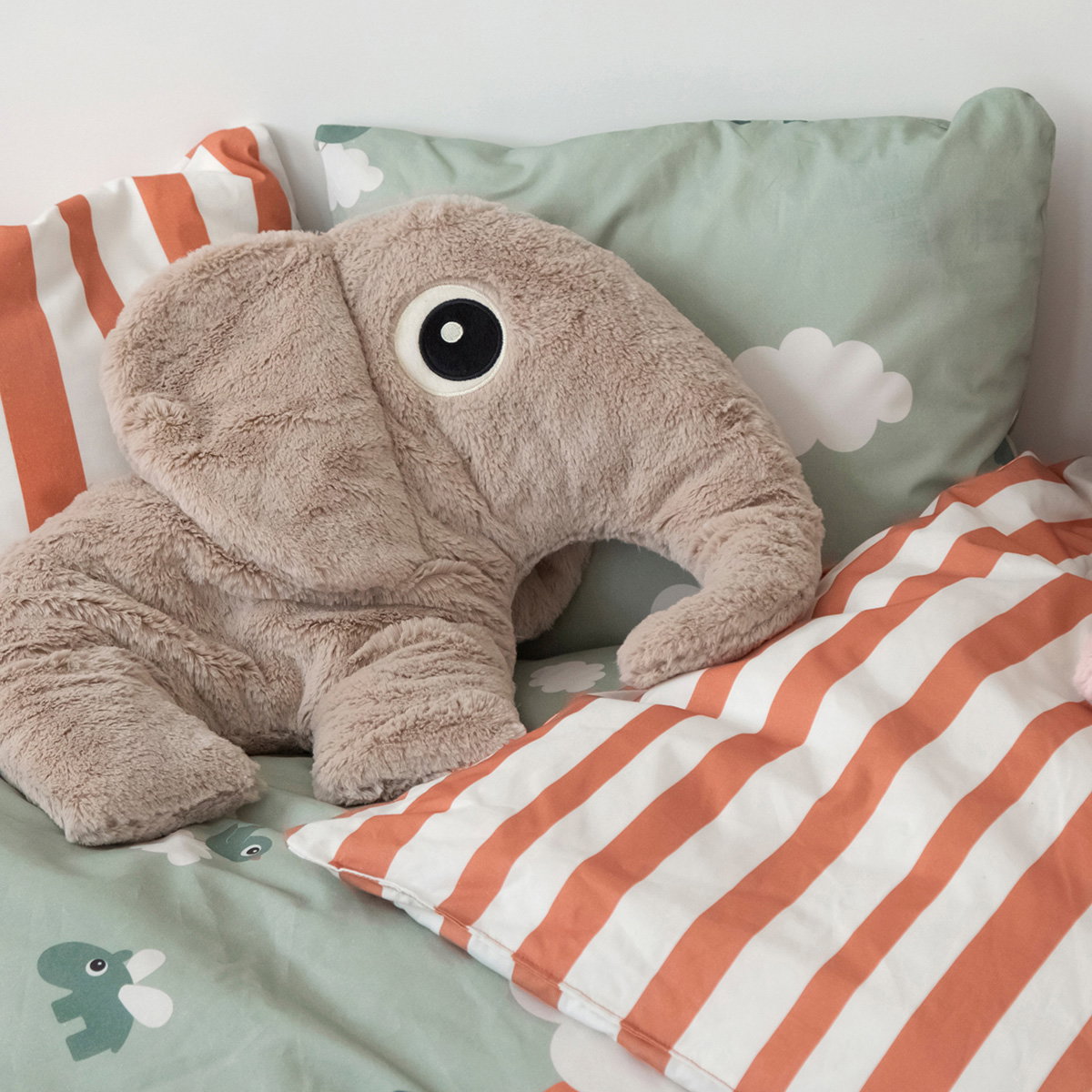 gosedjur elefant beige liggandes på säng med randig kudde och molnmönster