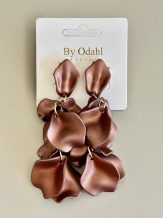 närbild på chokladbruna örhängen i lövform hängande på ett vitt kort med texten by odahl