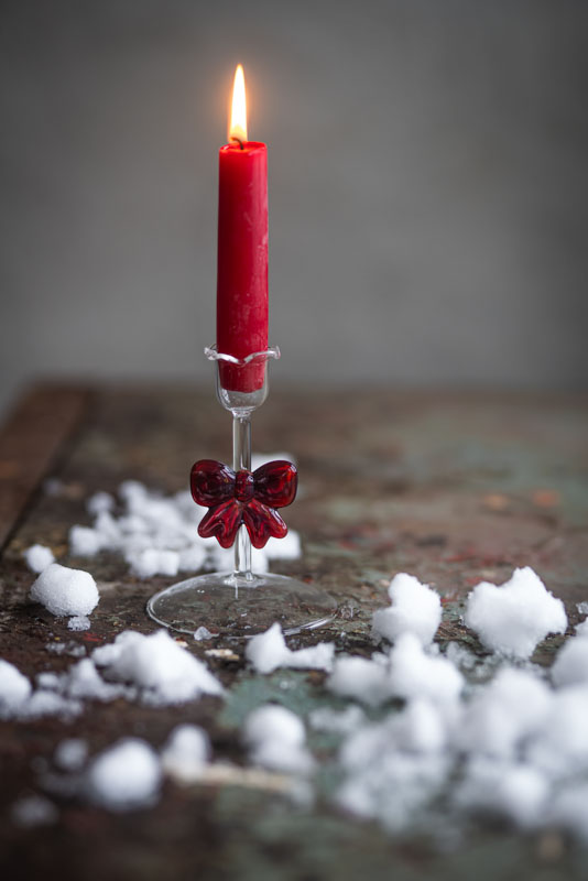 ljusstake rosett glas med brinnande rött ljus och röd glassrosett på en yta med snöliknande dekorationer
