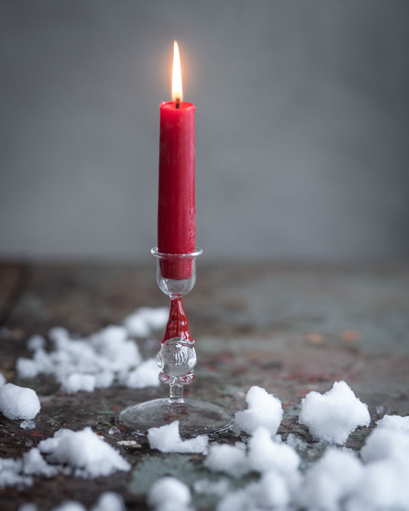 tomte ljusstake glas med tänt rött ljus på rustik yta omgiven av konstsnö