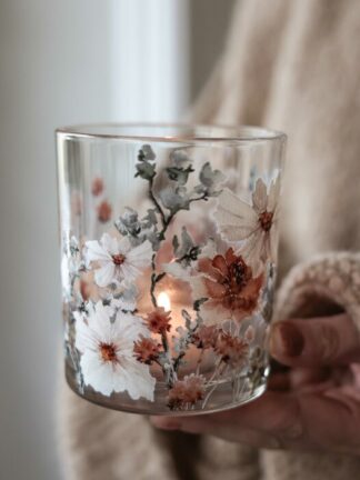 Majas lykta anemone i glas med vita och rostfärgade anemoner och ett tänd värmeljus, hålls i en hand
