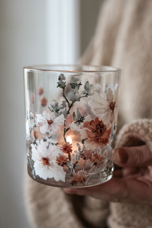 majas lykta anemone i glas med vita och rostfärgade anemoner och ett tänd värmeljus, hålls i en hand