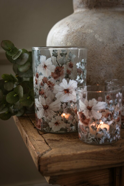 majas lykta anemone i två glaslyktor med vita och rostfärgade anemoner, tända värmeljus på ett träbord med eucalyptus och en vas i bakgrunden.