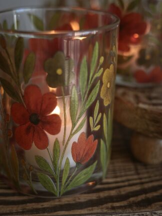 Närbild på ljuslykta med blommor i glas med handmålade röda och gula blommor och ett tänd värmeljus inuti