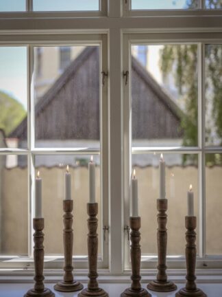 rustik ljusstake trä i olika höjder på en fönsterbräda med tända vita kronljus framför ett spröjsat fönster
