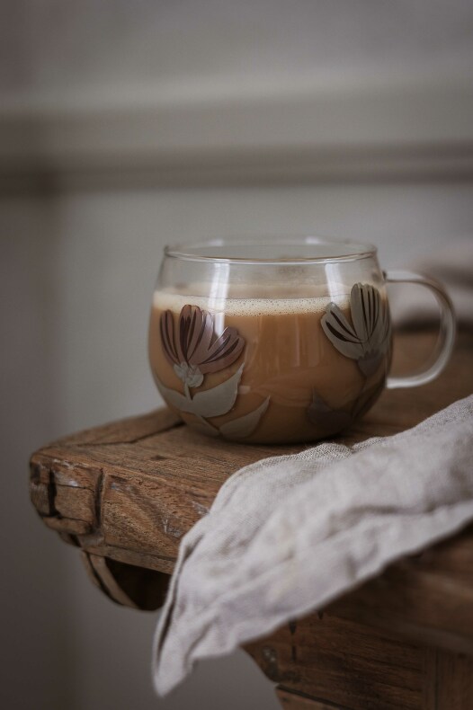 majas glasmugg blomia i glas med blommönster, fylld med latte på en rustik träyta