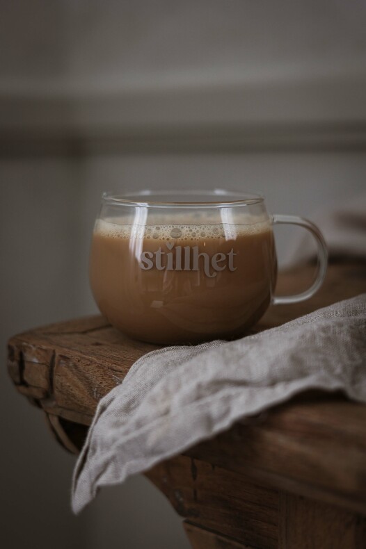 majas glasmugg stillhet fylld med kaffe på ett rustikt träbord intill en linneservett