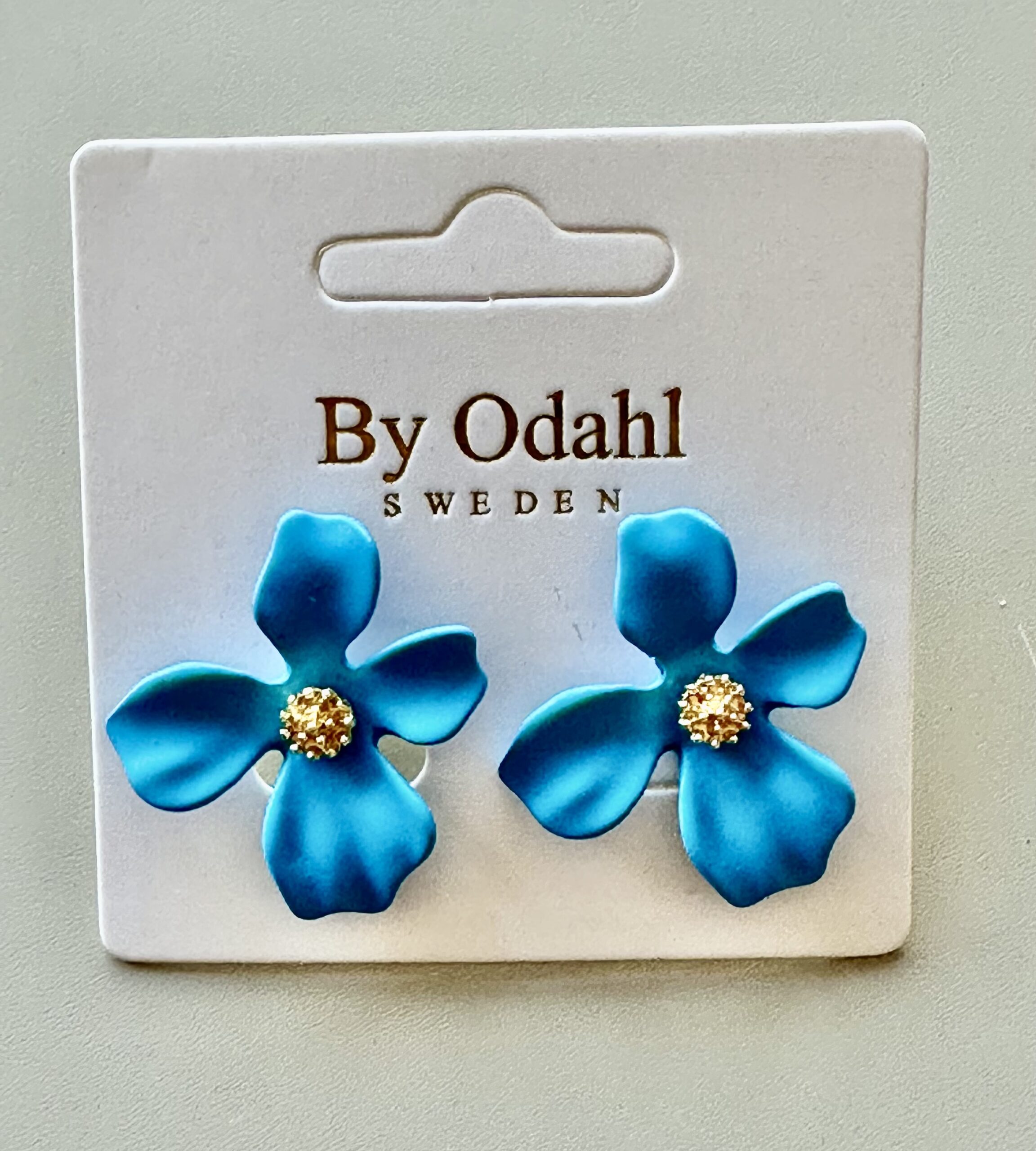 närbild av blå blomma örhängen på ett vitt monteringskort med texten 'by odahl sweden'.