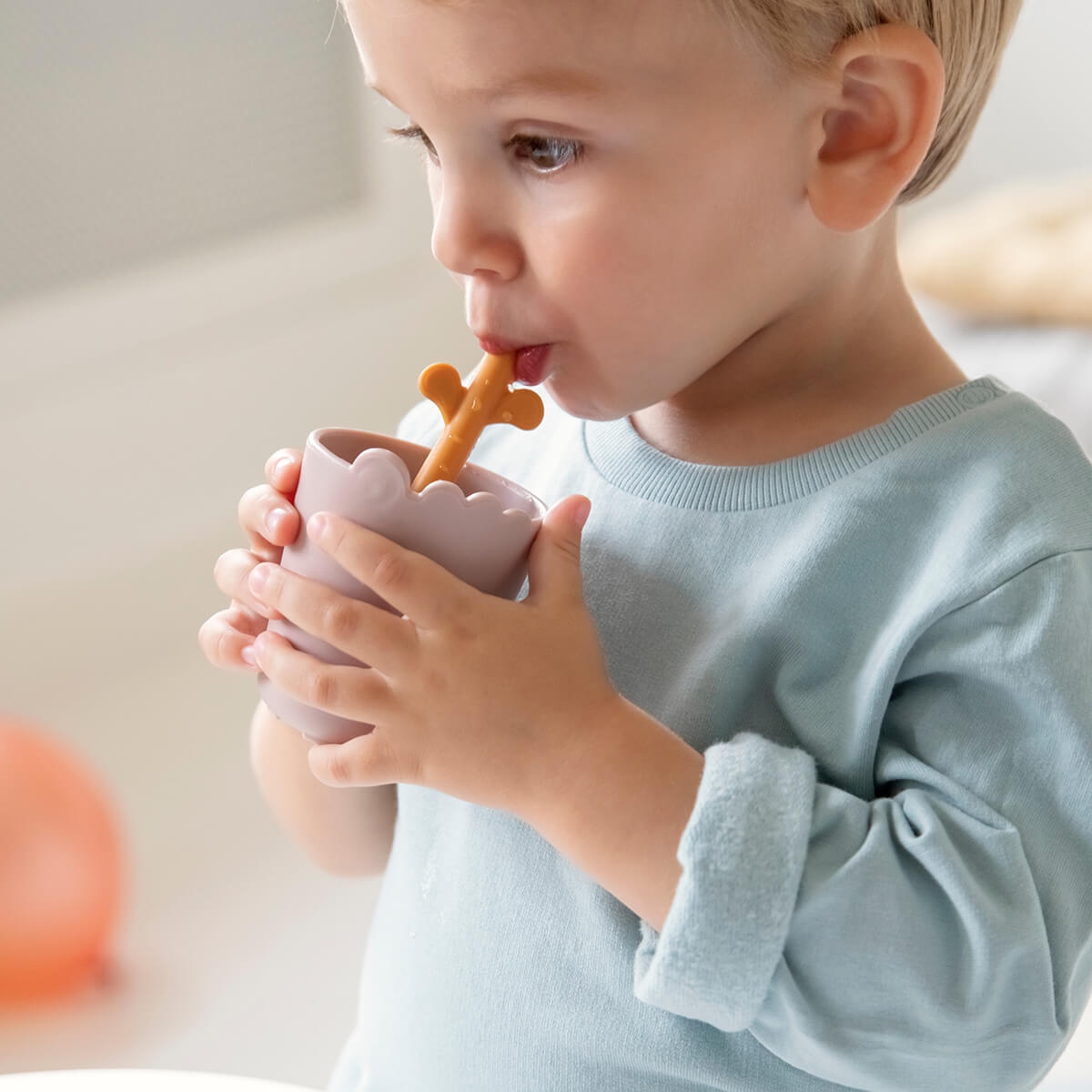 barnmugg kiddish croco powder i ljusrosa med orange sugrör, hållen av ett barn